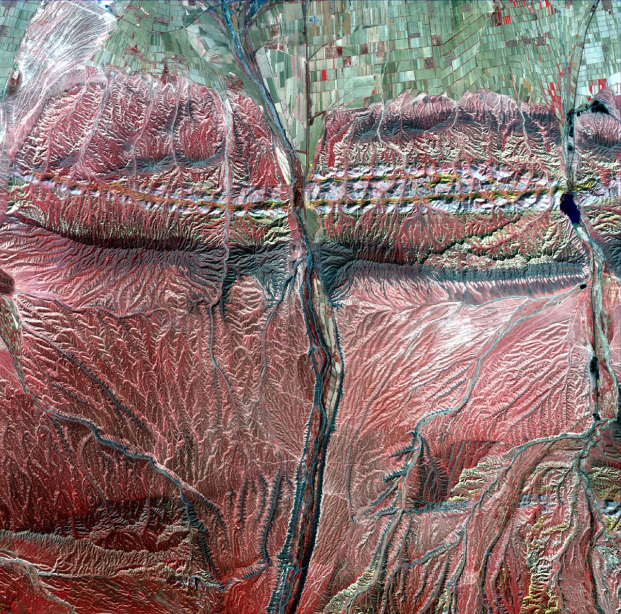 "Muscles" of the Changji Hutubi Valley. Taken on April 20, 2014, green farmland is seen above with mountains (red) worn by water erosion below.